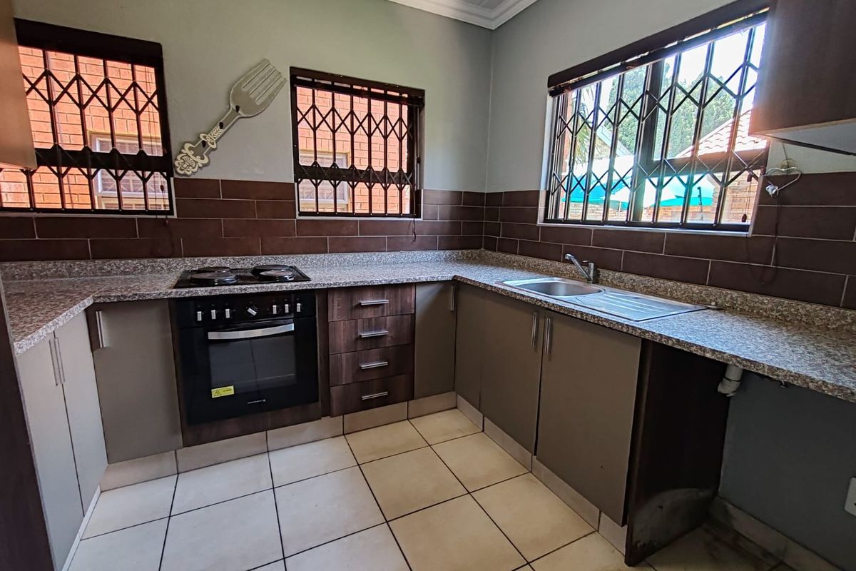 A functional kitchen featuring built-in cabinetry, a hob, an oven, tiled splashbacks, and tiled flooring, with security bars installed on the windows.