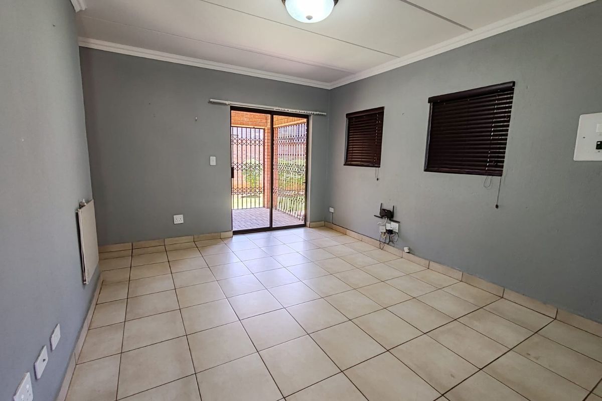 An empty living room featuring neutral tiled flooring, grey walls, a wall-mounted heater, and a sliding door leading to an outdoor patio area.