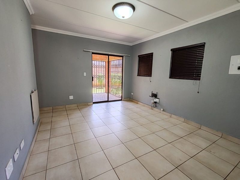 An empty living room featuring neutral tiled flooring, grey walls, a wall-mounted heater, and a sliding door leading to an outdoor patio area.