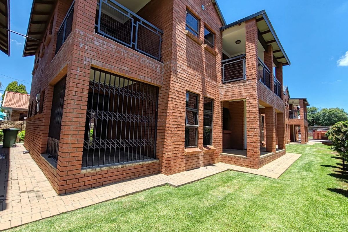 Rear view of a multi-story apartment building featuring face brick construction, private balconies with metal railings, and a well-maintained lawn area.