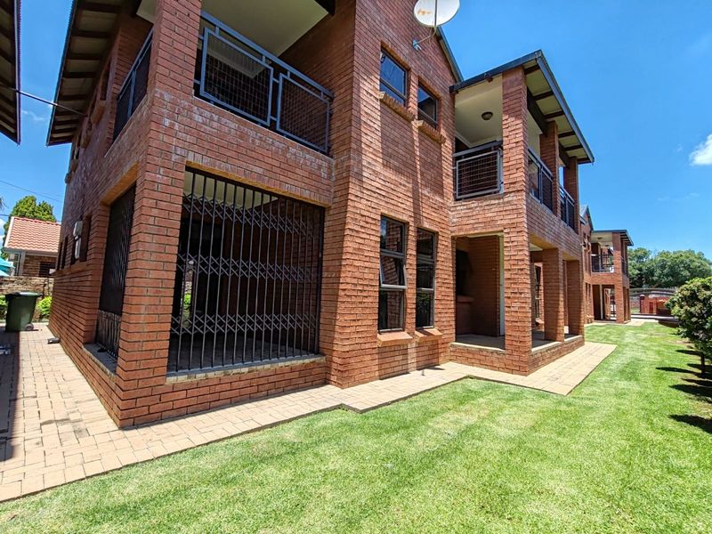 Rear view of a multi-story apartment building featuring face brick construction, private balconies with metal railings, and a well-maintained lawn area.