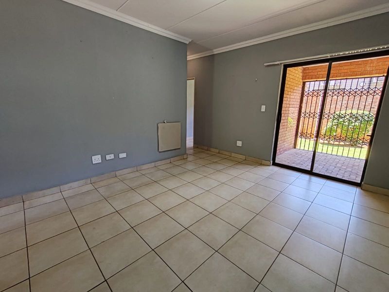 An empty living room featuring tiled flooring, a wall-mounted heater, and a sliding glass door providing access to an outdoor patio area.