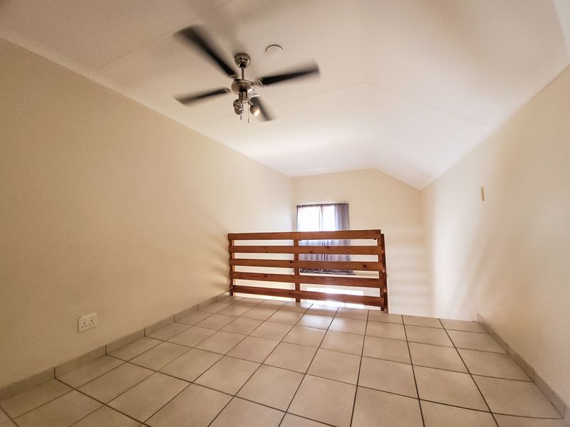 An empty loft-style bedroom featuring tiled flooring, a vaulted ceiling with a fan, and a wooden balustrade overlooking the lower level.