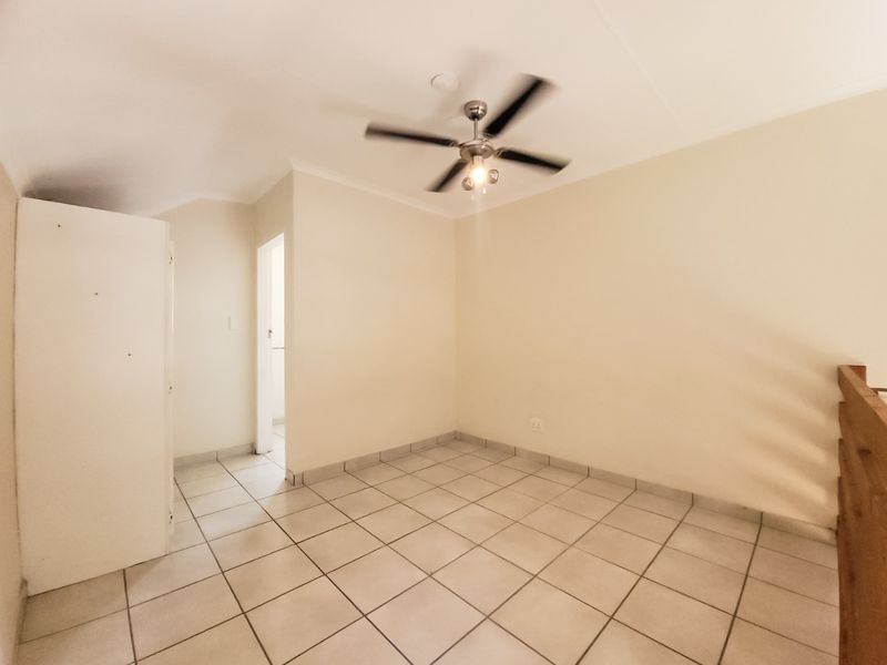 An empty bedroom featuring tiled flooring, a ceiling fan, and a built-in cupboard, with a wooden balustrade overlooking the lower level.