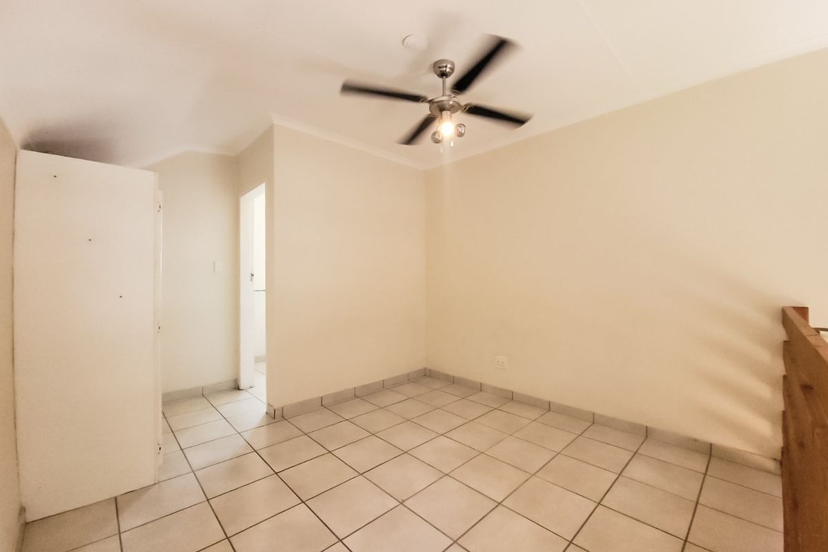 An empty bedroom featuring tiled flooring, a ceiling fan, and a built-in cupboard, with a wooden balustrade overlooking the lower level.