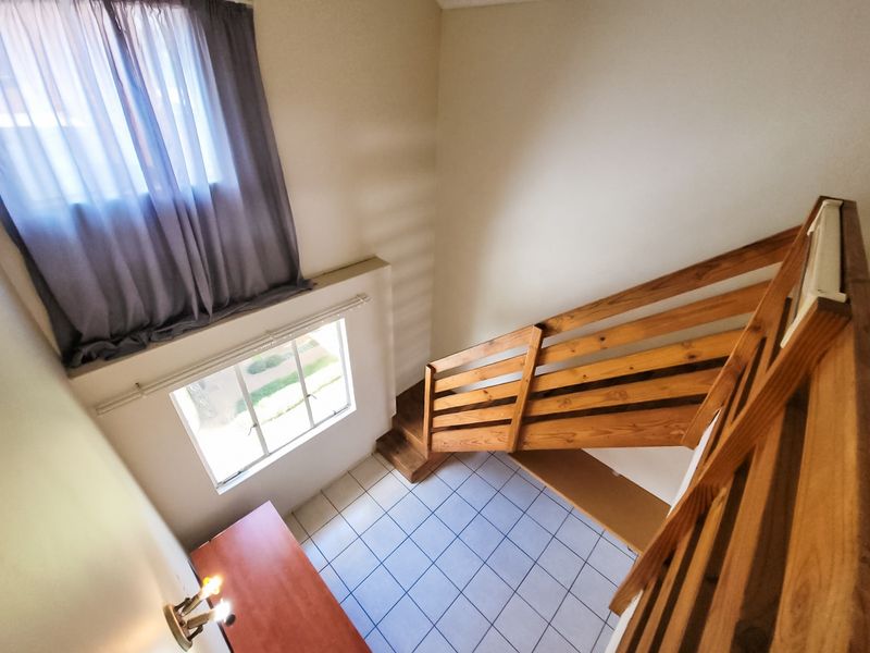 A bright, open-plan hallway featuring a wooden staircase, tiled flooring, and a large window providing natural light.