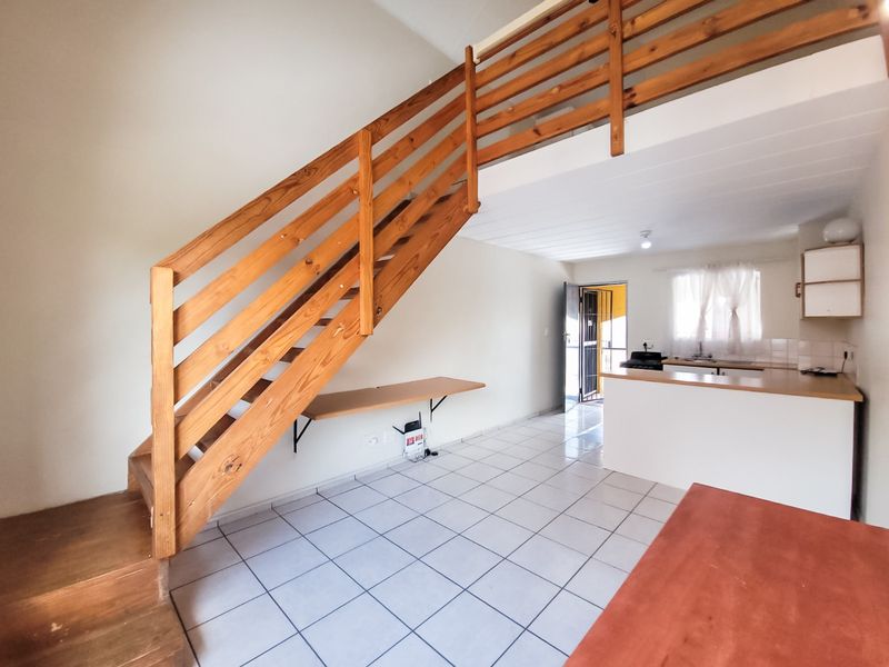 Open-plan living area featuring a wooden staircase, tiled flooring, and a functional kitchen space with built-in cabinetry and countertops.