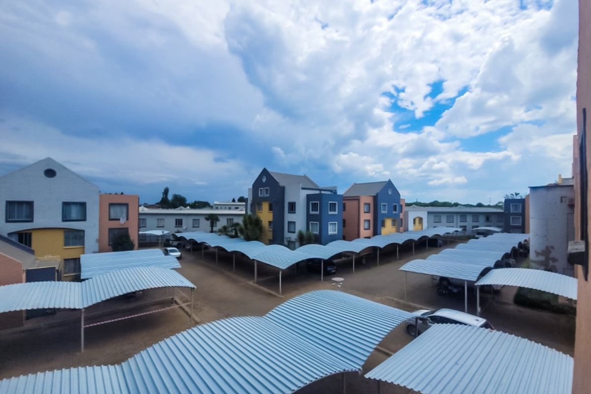 An elevated view of an apartment complex courtyard featuring extensive covered parking bays and multi-story residential buildings under a cloudy sky.