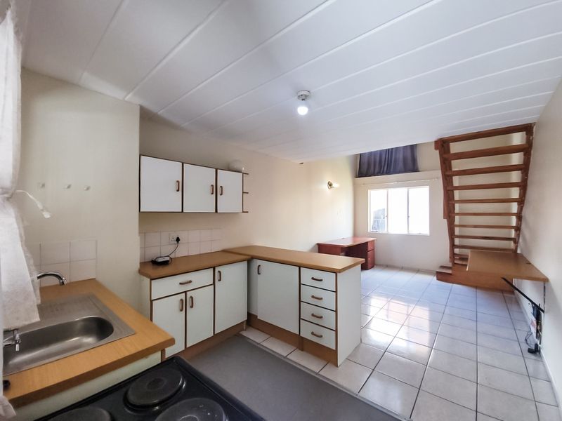 Open-plan kitchen and living area featuring tiled floors, functional cabinetry, and a wooden staircase leading to an upper level.