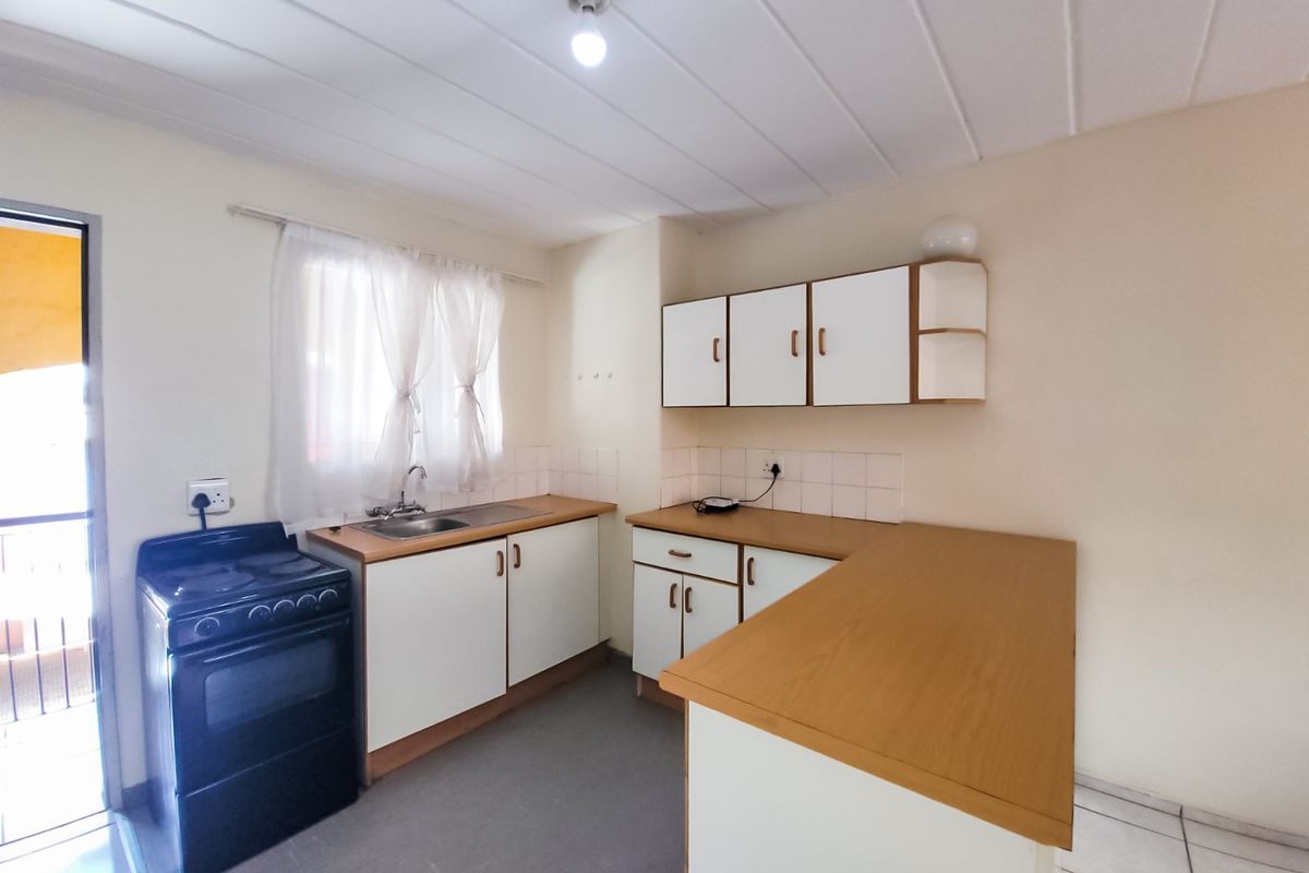 A functional kitchen featuring white cabinetry, laminate countertops, a stainless steel sink, and a freestanding stove, offering a clean and practical layout.