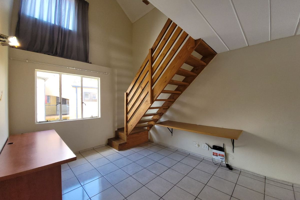 Spacious living area featuring a wooden staircase, vaulted ceilings, tiled flooring, and a built-in desk, offering a bright and open layout.