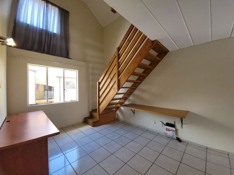 Spacious living area featuring a wooden staircase, vaulted ceilings, tiled flooring, and a built-in desk, offering a bright and open layout.