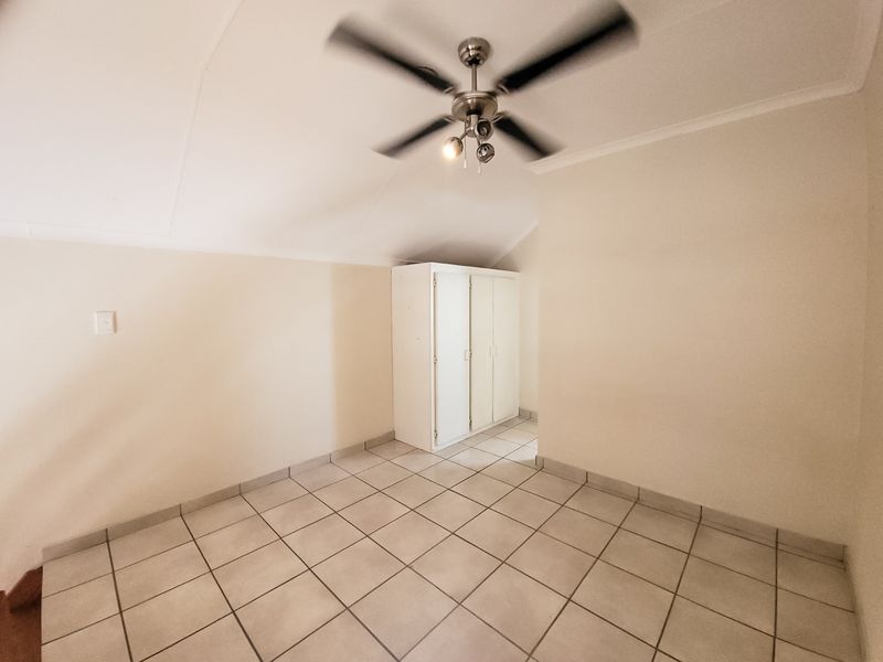 A bright, empty bedroom featuring neutral tiled flooring, a ceiling fan, and a built-in cupboard for storage.
