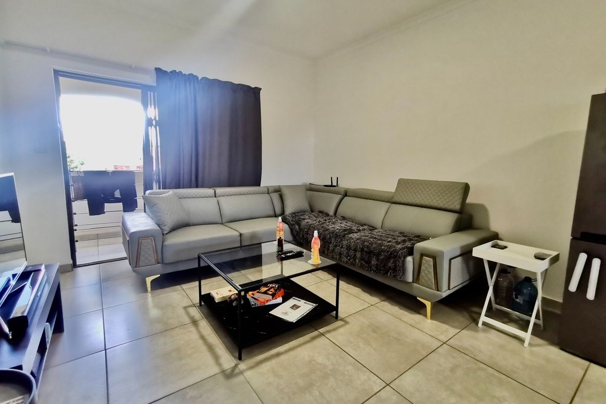 A living room featuring neutral tiled flooring and a sliding glass door providing access to an outdoor balcony area.