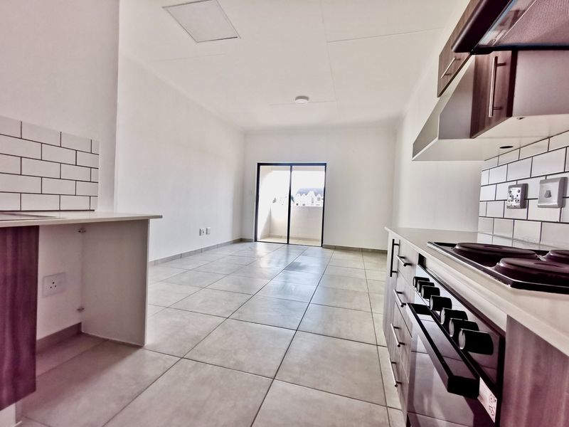 An open-plan kitchen and living area featuring modern cabinetry, a built-in stove, subway tile backsplash, and direct access to a balcony.