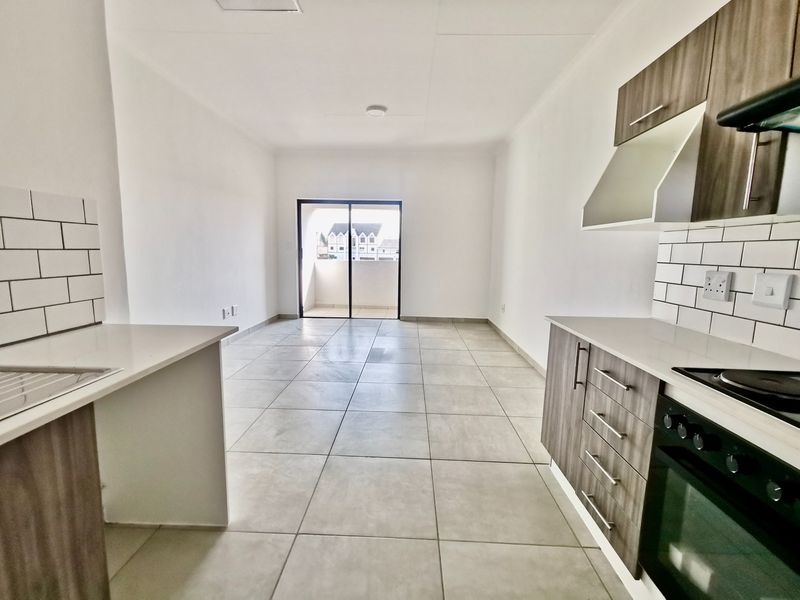 Modern open-plan kitchen and living area featuring neutral tiled flooring, contemporary cabinetry, and a sliding door leading to a balcony.