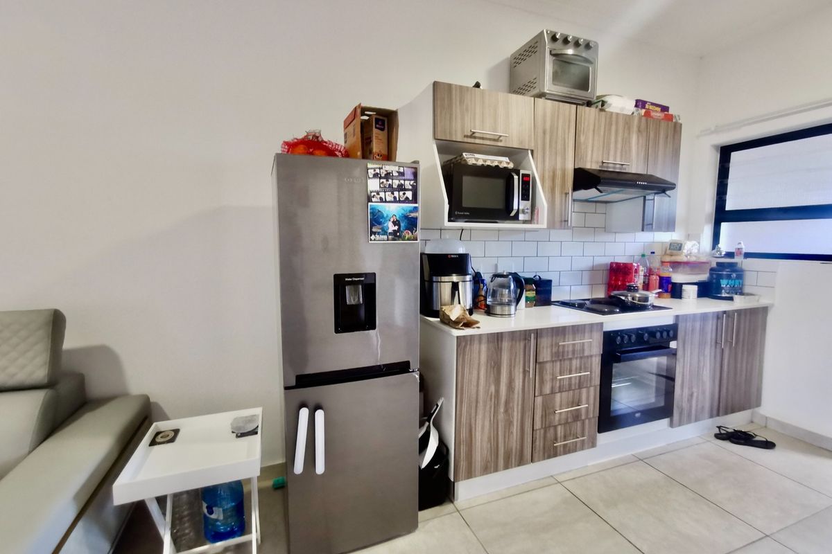 A functional kitchen featuring wood-grain cabinetry, subway tile backsplash, integrated oven, hob, and extractor fan, with tiled flooring throughout.