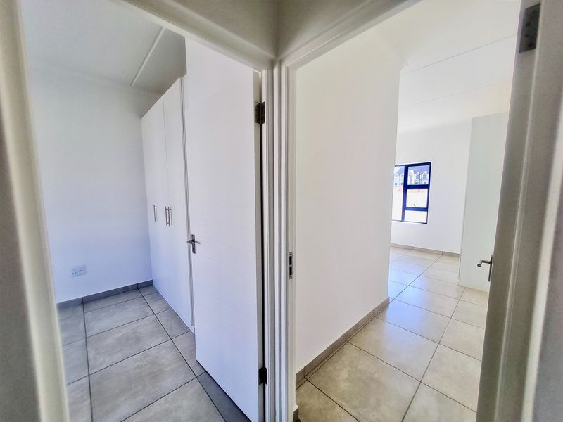 A bright, neutral hallway featuring tiled flooring and built-in cupboards, providing clean, modern access between rooms in this apartment.