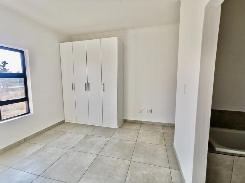 A bright, empty bedroom featuring neutral tiled flooring, a modern built-in wardrobe, and a large window providing natural light.