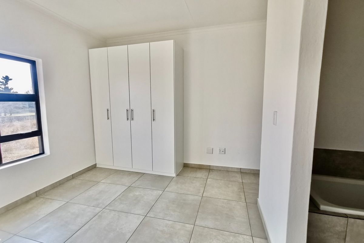 A bright, empty bedroom featuring neutral tiled flooring, a modern built-in wardrobe, and a large window providing natural light.
