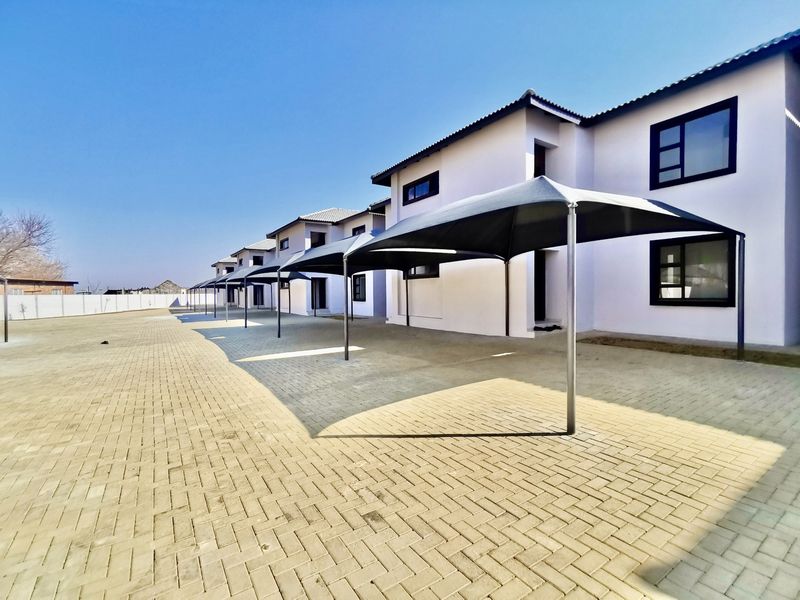 Exterior view of a modern apartment complex featuring a paved driveway and dedicated shade cloth carport parking bays.