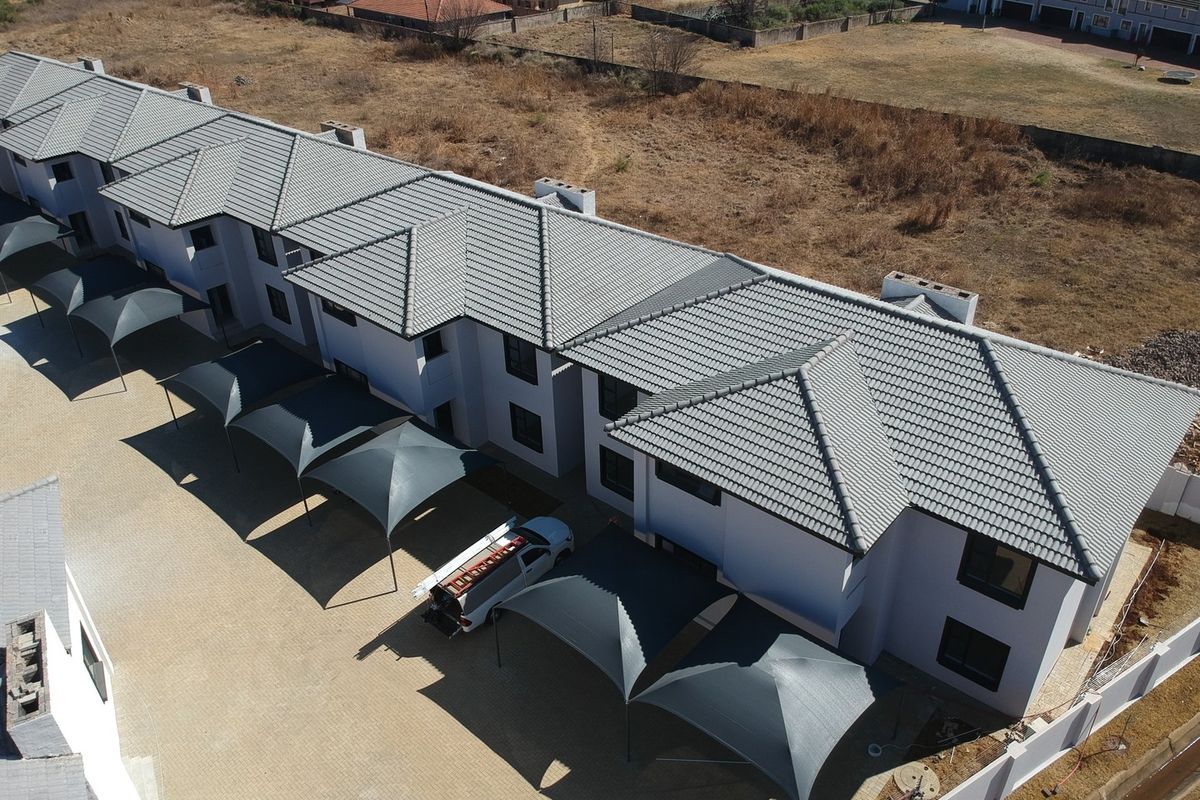 Aerial view of a modern apartment complex featuring a tiled roof, paved driveway, and multiple shade cloth carports.