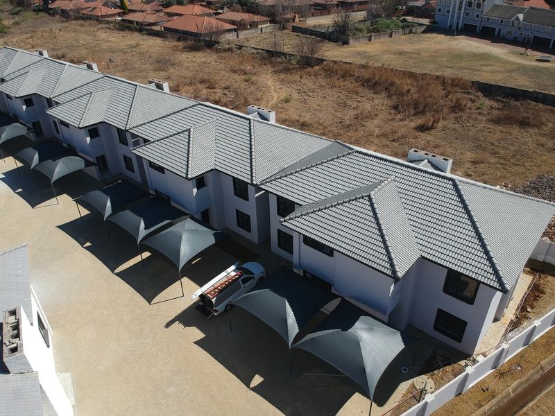 Aerial view of a modern apartment complex featuring a tiled roof, paved driveway, and multiple shade cloth carports.