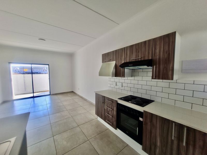 Modern open-plan kitchen and living area featuring contemporary wood-finish cabinetry, stone countertops, subway tile backsplash, and direct access to an outdoor space.