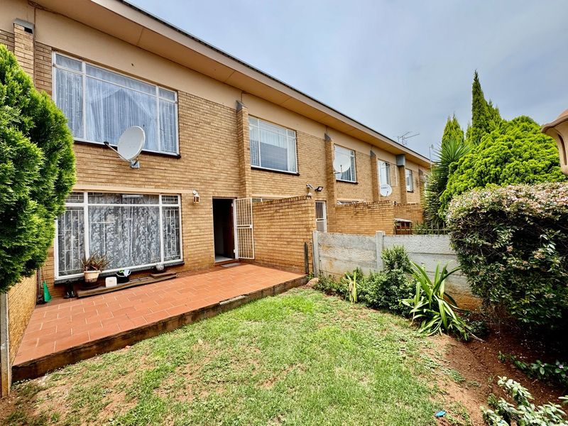 Rear view of a townhouse featuring a brick facade, a tiled patio area, and a private garden space with boundary walling.