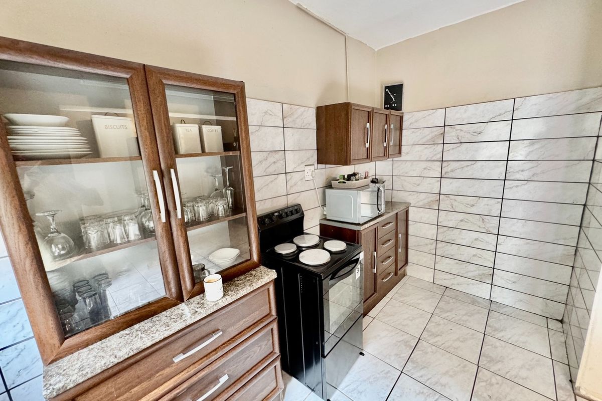 A functional kitchen featuring wooden cabinetry, granite countertops, a freestanding stove, and full-height marble-look wall tiling.