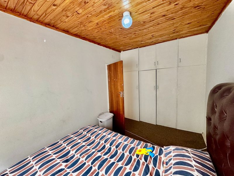A bedroom featuring built-in cupboards, a timber-clad ceiling, and carpeted flooring, offering a functional space with potential for cosmetic updates.