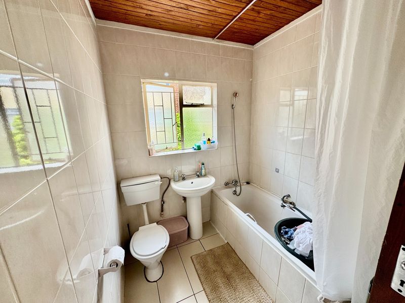 A compact bathroom featuring a pedestal basin, toilet, and bathtub with a handheld shower mixer, finished with tiled walls and a timber ceiling.
