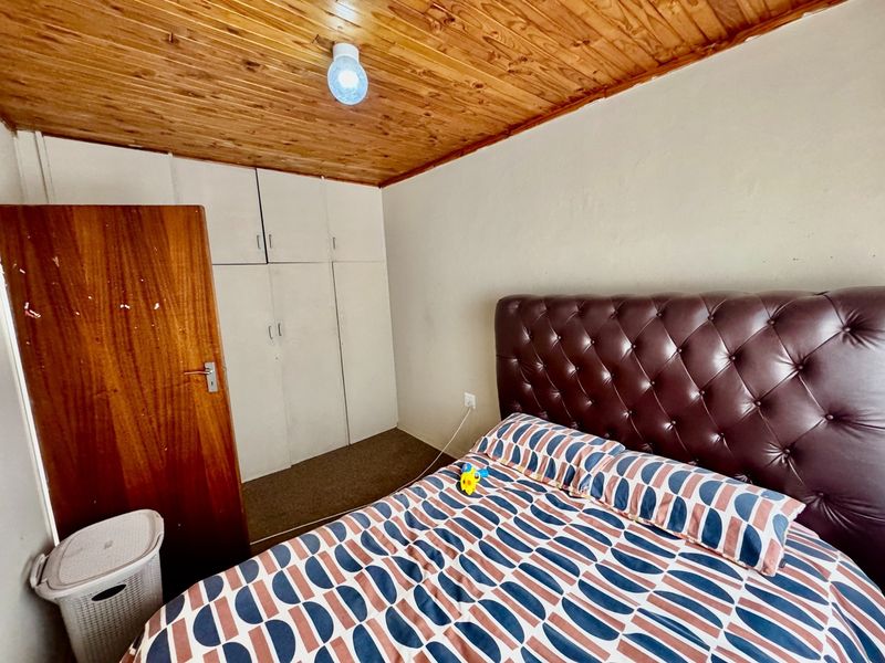 A bedroom featuring a timber ceiling, built-in storage cupboards, and a solid core door, requiring cosmetic updates to improve the overall finish.
