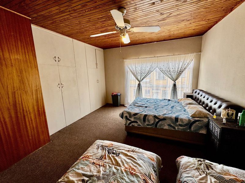 Spacious bedroom featuring built-in cupboards, a timber-paneled ceiling with a fan, and carpeted flooring.
