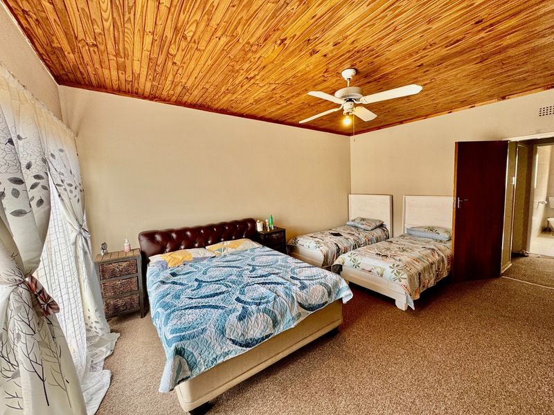 Spacious bedroom featuring a warm timber tongue and groove ceiling, ceiling fan, and carpeted flooring, with direct access to an en-suite bathroom.
