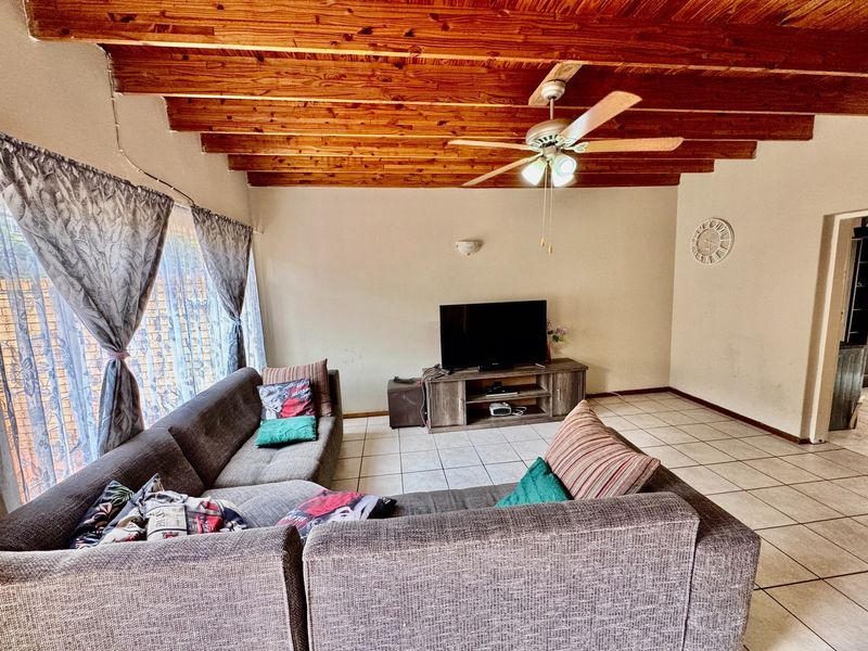Living room featuring exposed timber beam ceilings, ceiling fan, and ceramic tiled flooring, offering a rustic aesthetic with potential for modern updates.