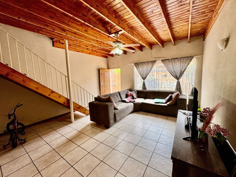 Spacious living room featuring exposed timber beam ceilings, tiled flooring, and a staircase, offering a functional layout with direct access to the exterior.