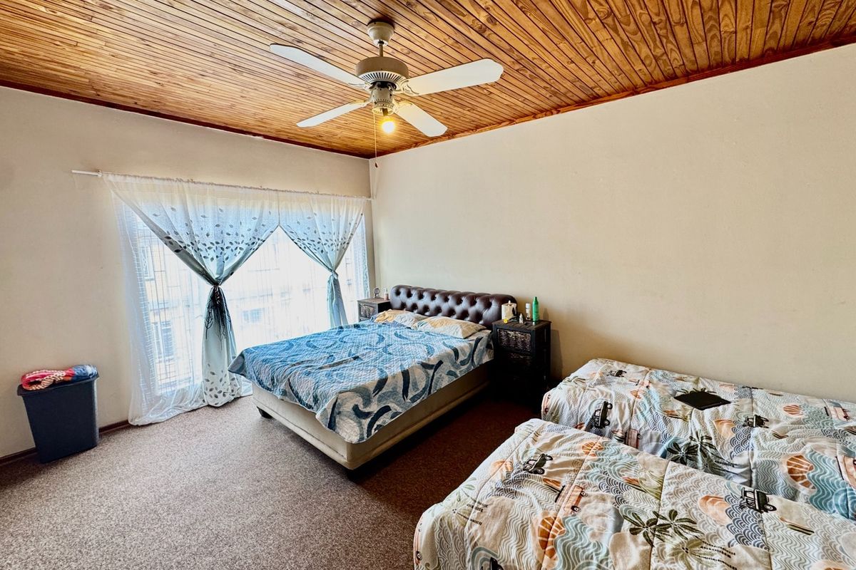 Spacious bedroom featuring a warm timber tongue and groove ceiling, a central ceiling fan, and carpeted flooring with large window access.