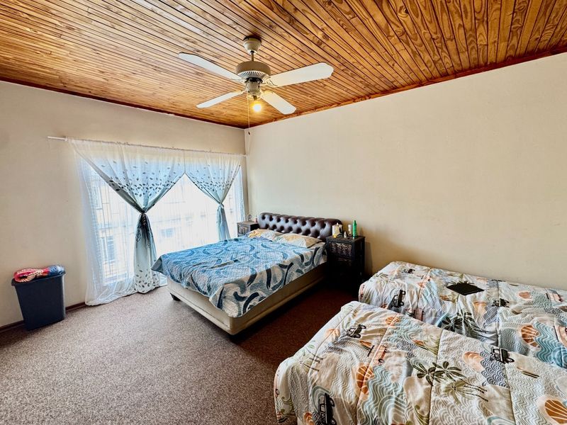 Spacious bedroom featuring a warm timber tongue and groove ceiling, a central ceiling fan, and carpeted flooring with large window access.