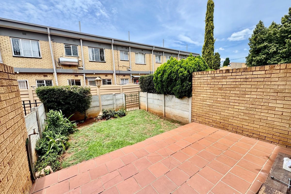 A private rear courtyard featuring a tiled patio area, a small lawn, and brick boundary walls, providing a functional outdoor space for the townhouse.