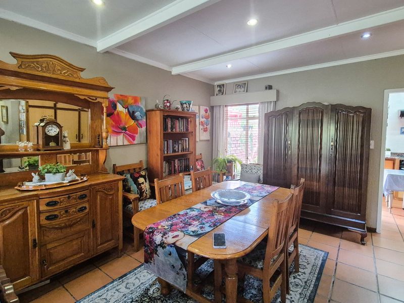 A dining room featuring tiled flooring, exposed ceiling beams, and recessed lighting, with an open transition to the adjacent kitchen area.