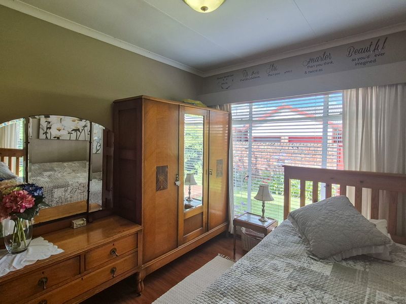 A well-lit bedroom featuring laminate flooring, large windows with venetian blinds, and classic cove cornicing, offering a comfortable and functional living space.