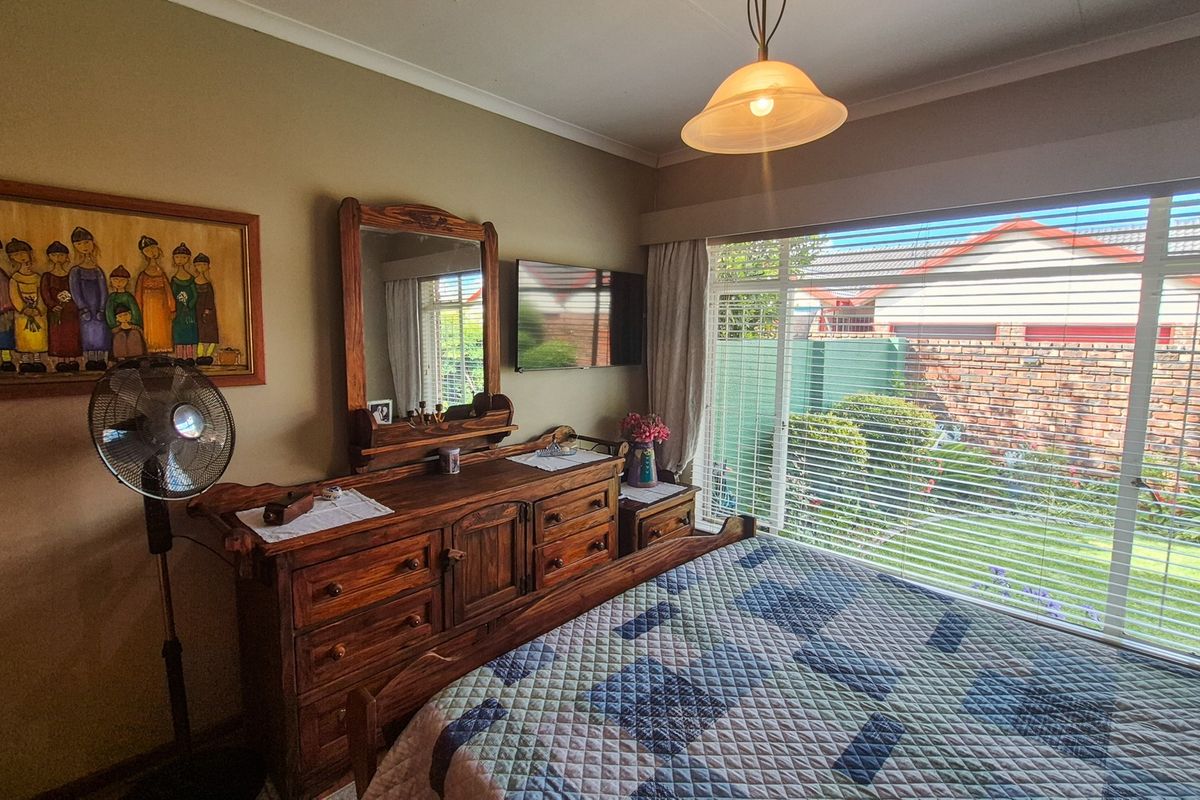 A well-lit bedroom featuring a large window with garden views, neutral wall tones, and classic cornice detailing.