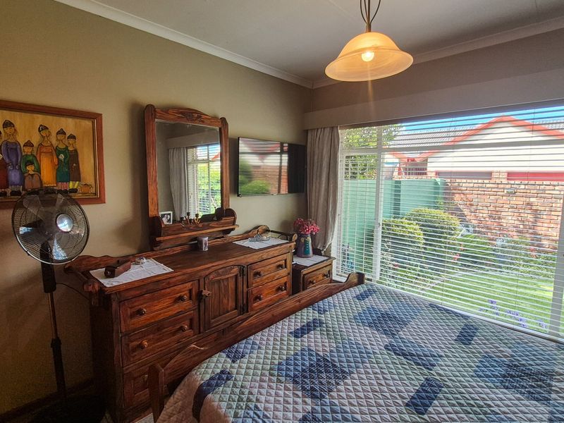 A well-lit bedroom featuring a large window with garden views, neutral wall tones, and classic cornice detailing.