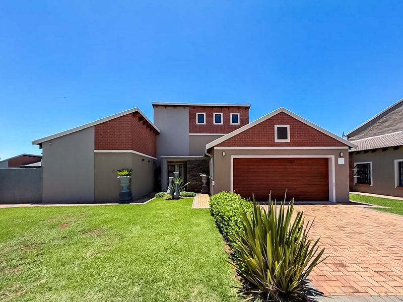 A well-maintained townhouse featuring a double garage, brick-paved driveway, and a neat front lawn with modern architectural brick and plaster finishes.
