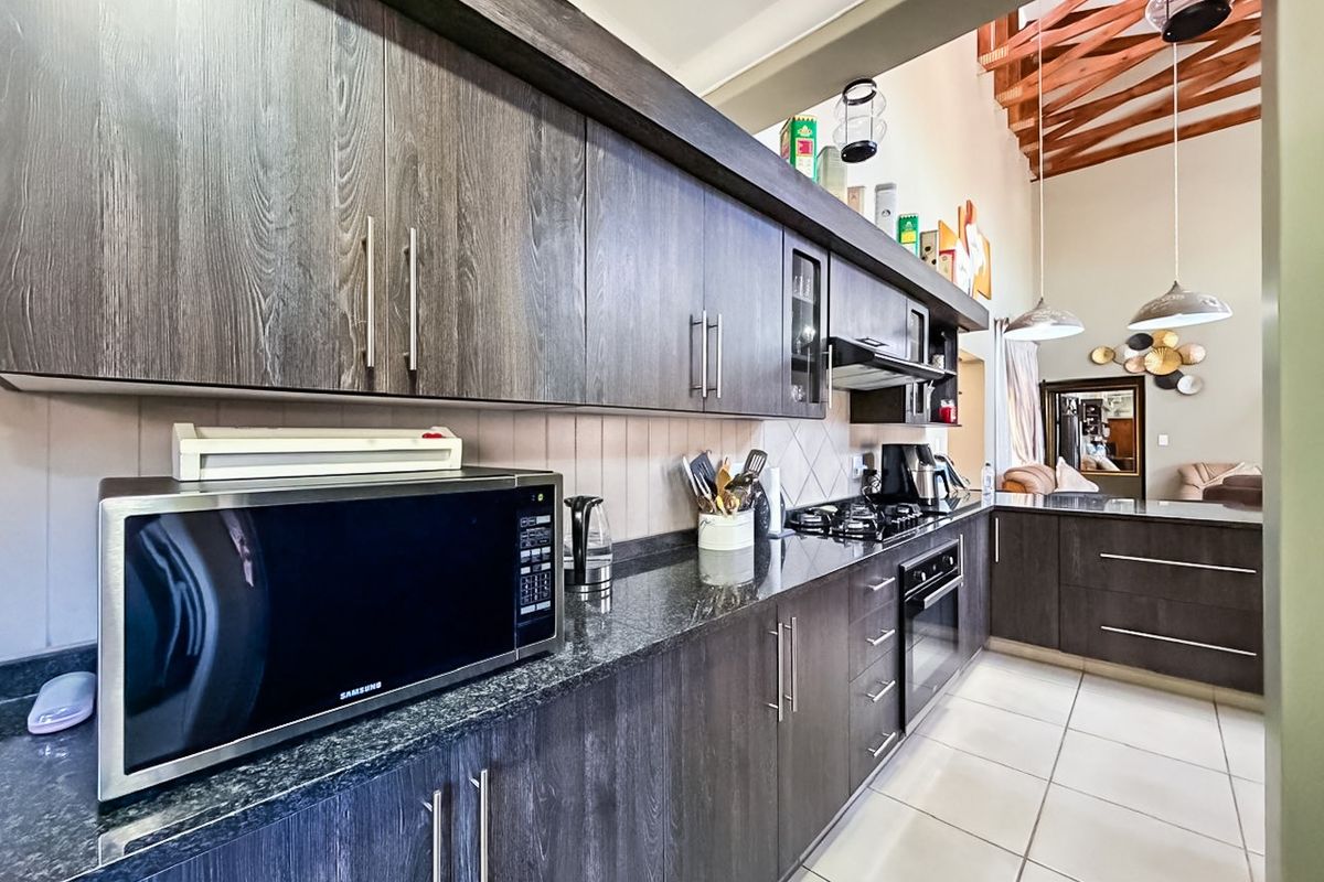 Modern kitchen featuring dark wood cabinetry, granite countertops, built-in gas hob, oven, and extractor fan, complemented by high ceilings with exposed timber trusses.