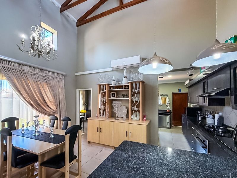 Spacious open-plan living and dining area featuring vaulted ceilings with exposed timber beams, modern kitchen with granite countertops, and integrated appliances.