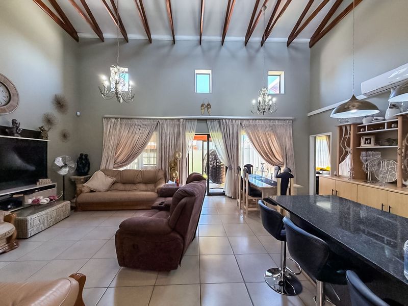 Spacious open-plan living and dining area featuring high vaulted ceilings with exposed timber beams, tiled floors, and a modern granite kitchen island.