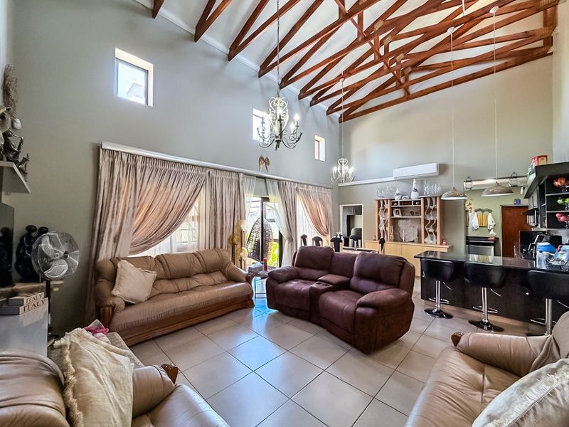 Spacious open-plan living area featuring high vaulted ceilings with exposed timber trusses, tiled floors, and an integrated kitchen with a breakfast island.