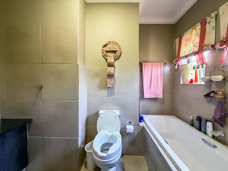 A functional bathroom featuring neutral wall tiles, a built-in bathtub, and a standard toilet, offering a clean and practical layout.